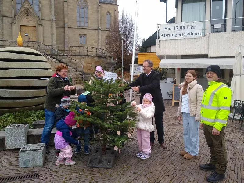 Erzieherinnen und Kinder der ev. Kindertagesstätte Gartenstraße schmücken zusammen mit Oberbürgermeister Sebastian Frei ihren Baum. Lea Richter vom Hauptamt und Bauhofleiter Achim Gerbig (rechter Bildrand) freuen sich über die gelungene Aktion.